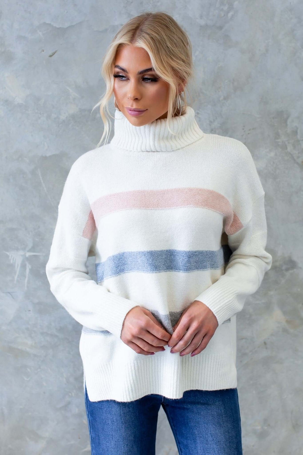 Model wearing a Lovey Jumper with turtle neckline and colorful stripes, styled with denim jeans against a textured background.