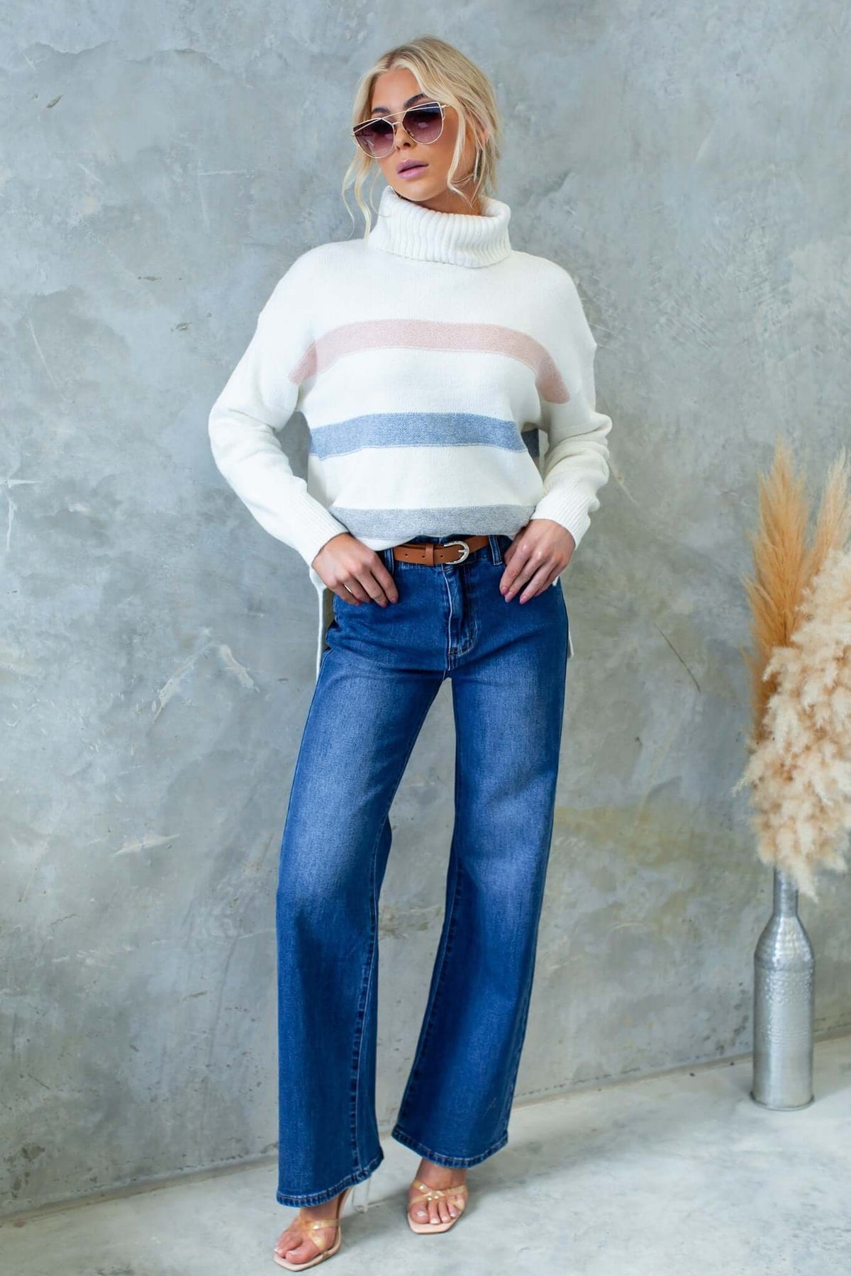 Model wearing Lovey Jumper with turtle neckline and side splits, paired with blue flared jeans and sunglasses.