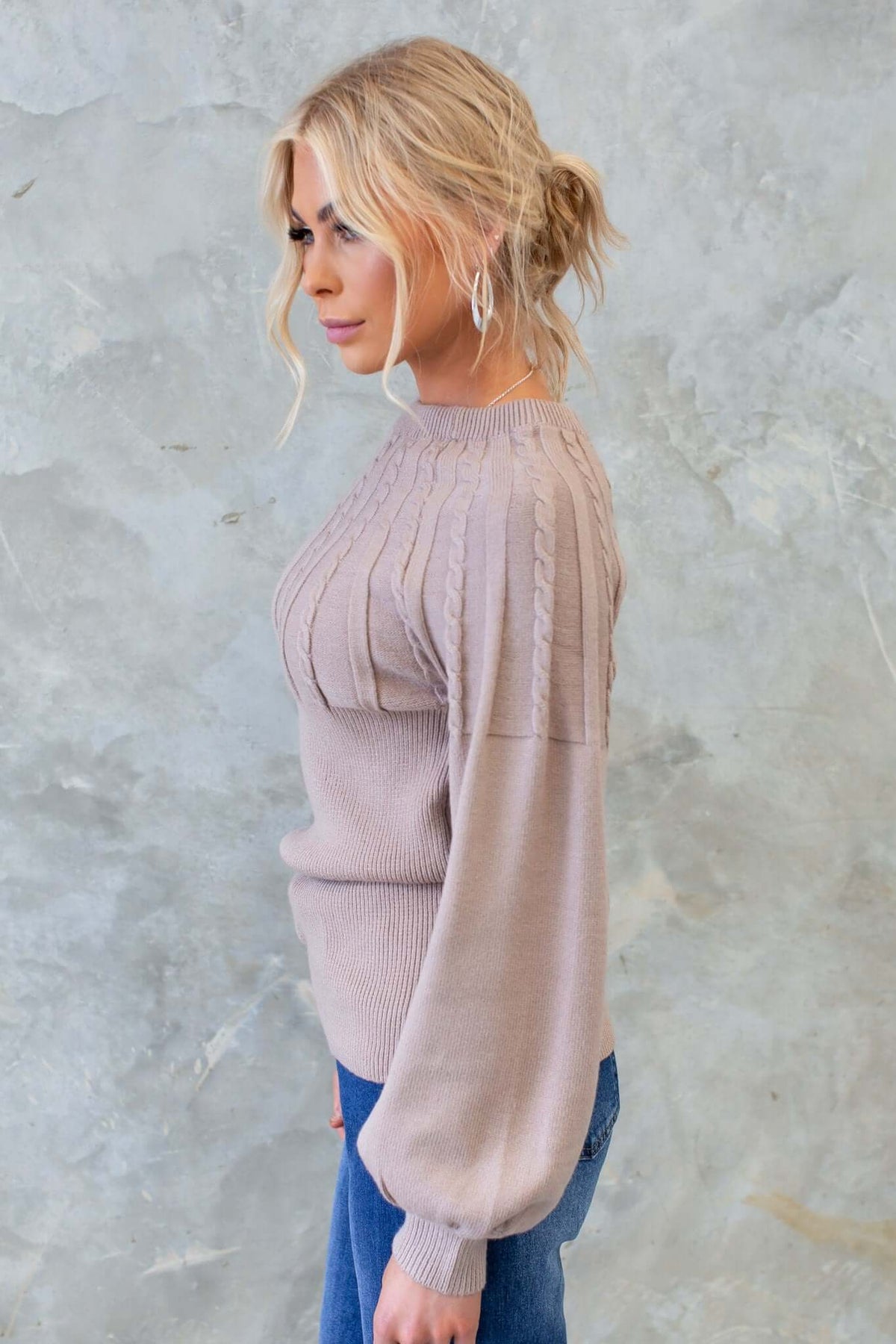 Side view of a model wearing the Alma Jumper, featuring a round neckline and cable knit design in a soft beige color.