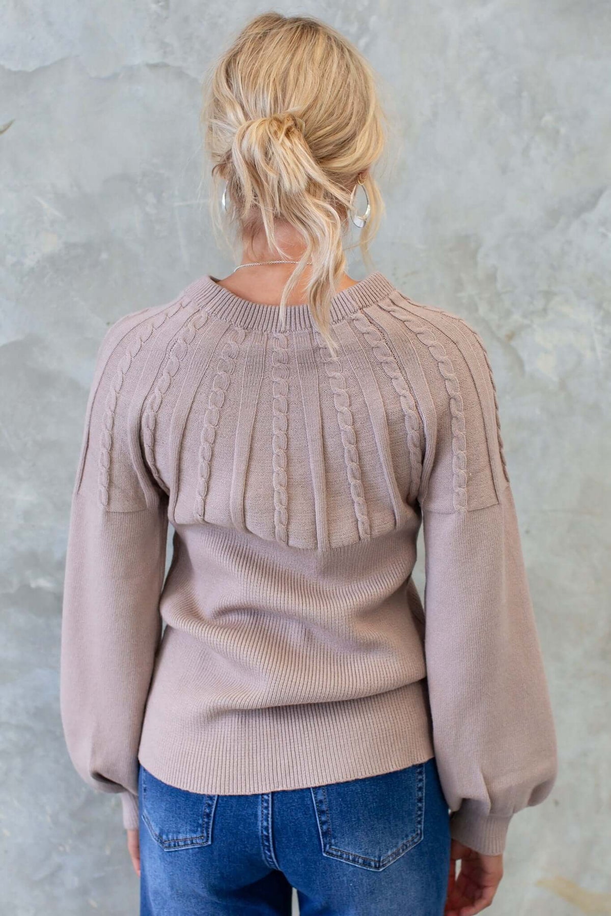 Back view of Alma jumper featuring cable knit design, round neckline and relaxed fit, styled with blue jeans.