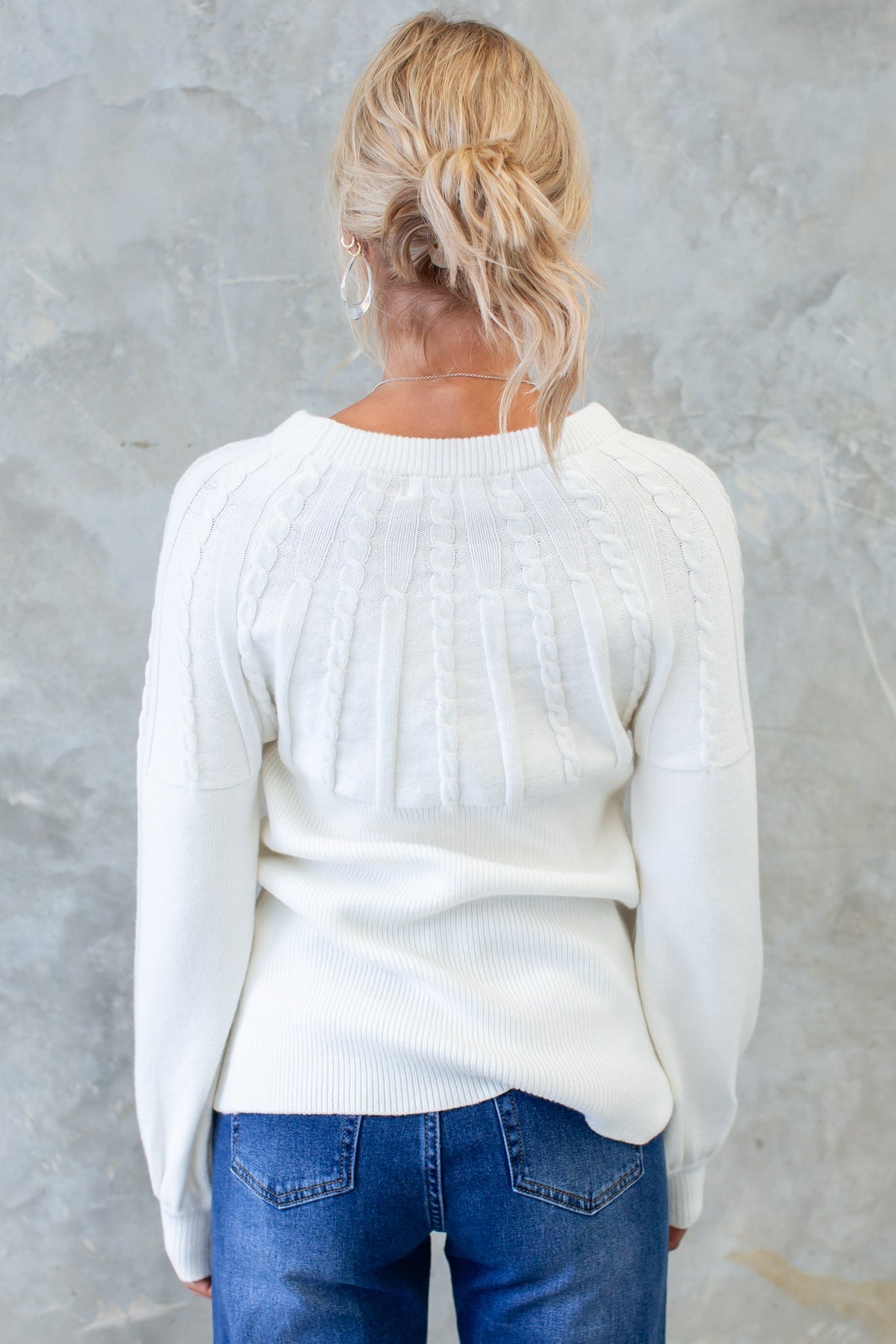 Back view of a woman wearing a white cable knit Alma Jumper with round neckline and relaxed fit.