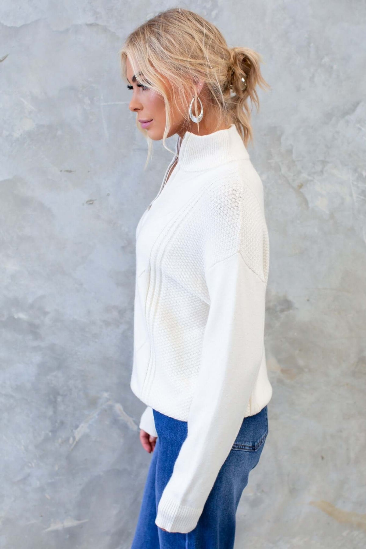 Side view of woman in white Tivoli Jumper with high neckline and 1/4 zip, styled with blue jeans.