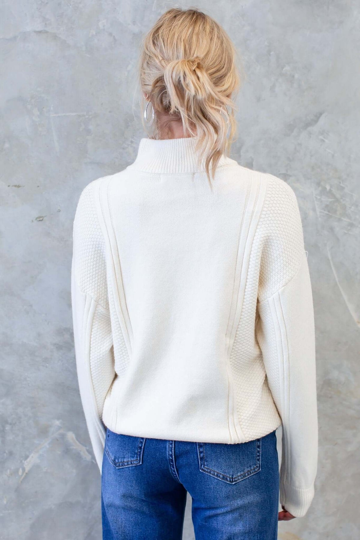 Back view of a woman wearing a cozy white Tivoli Jumper with a high neckline and relaxed fit.