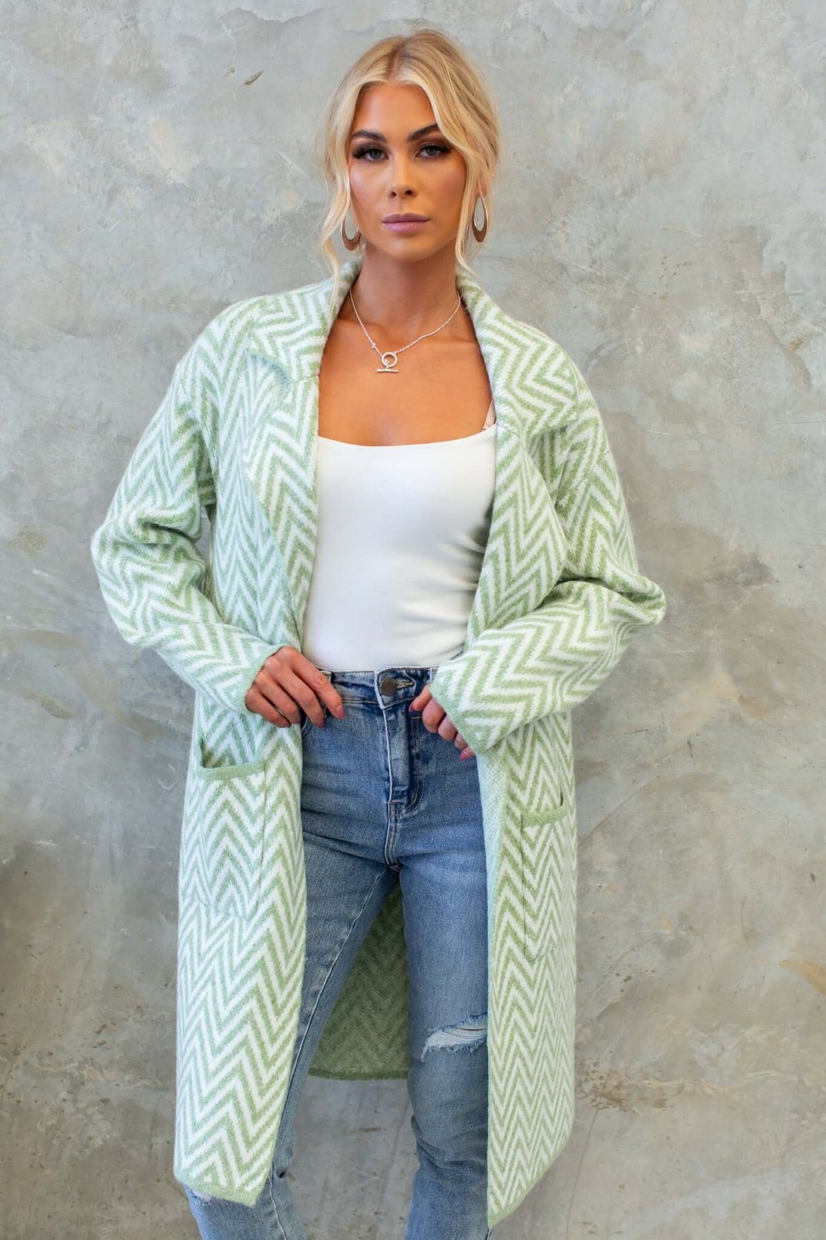Model wearing a longline Adabella cardigan in mint green herringbone knit with pockets, styled over a white top and jeans.