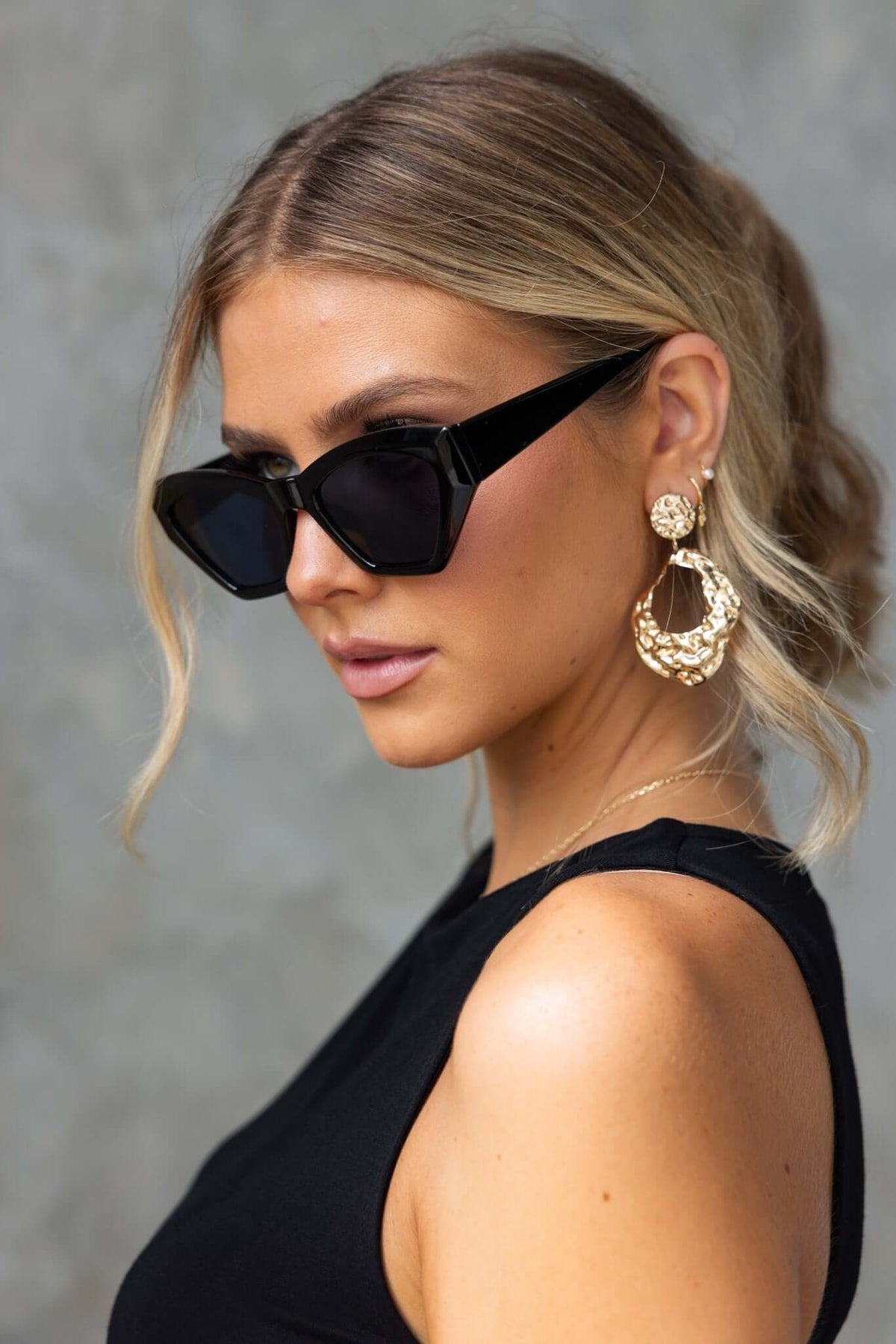 Woman wearing stylish black sunglasses and bold gold earrings, showcasing a trendy fashion look.