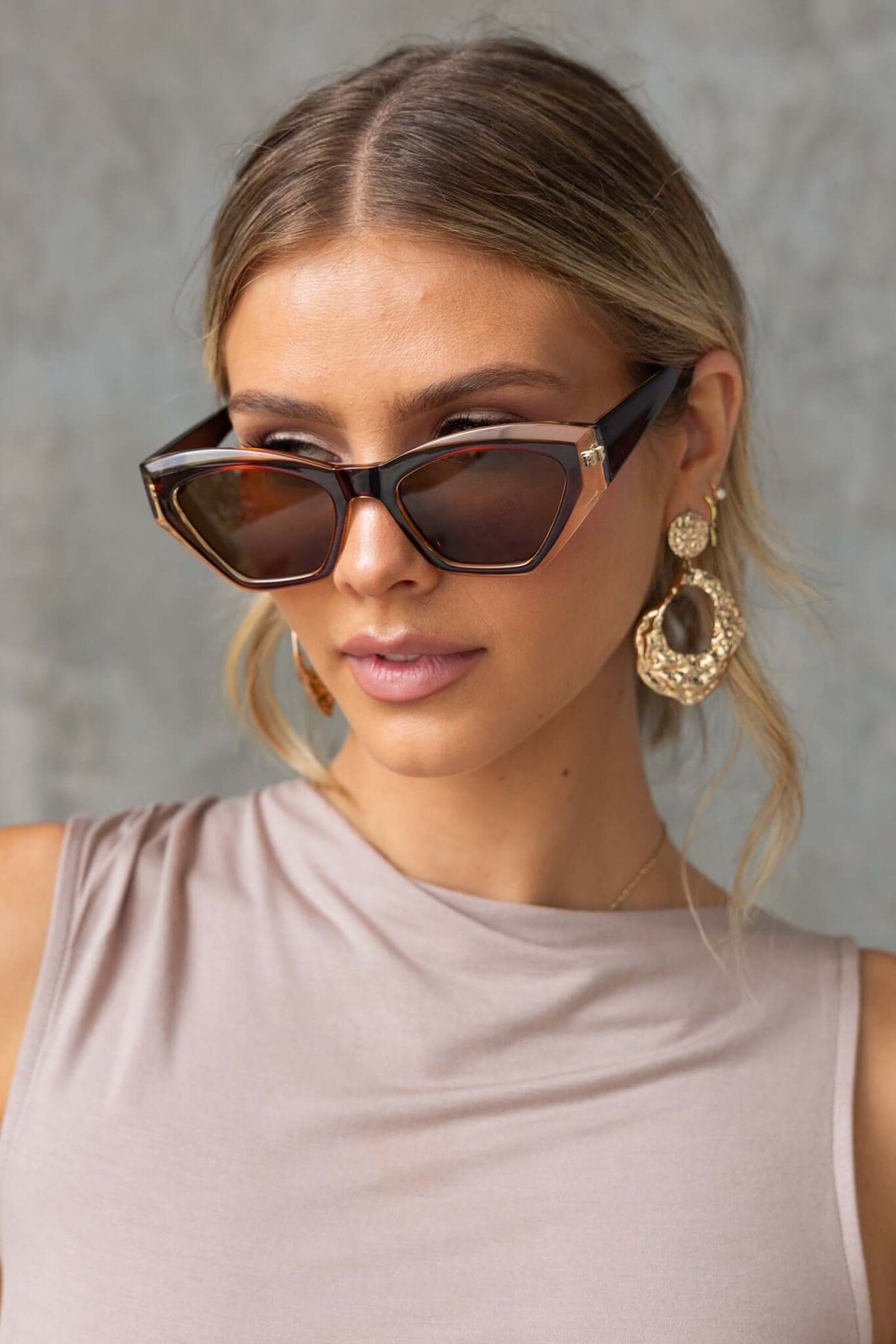Stylish woman wearing trendy brown-tinted sunglasses with fashionable earrings.