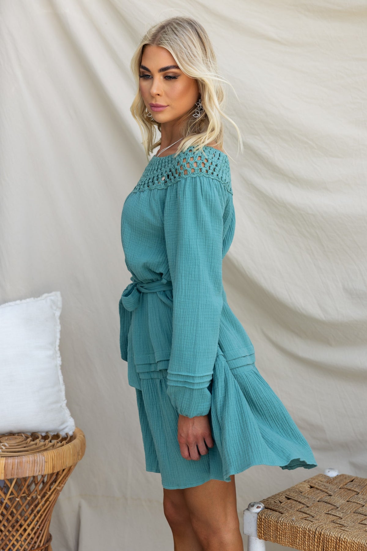 Model wearing the Hejda Dress in teal, featuring boat neckline, crochet detail, and removable tie.