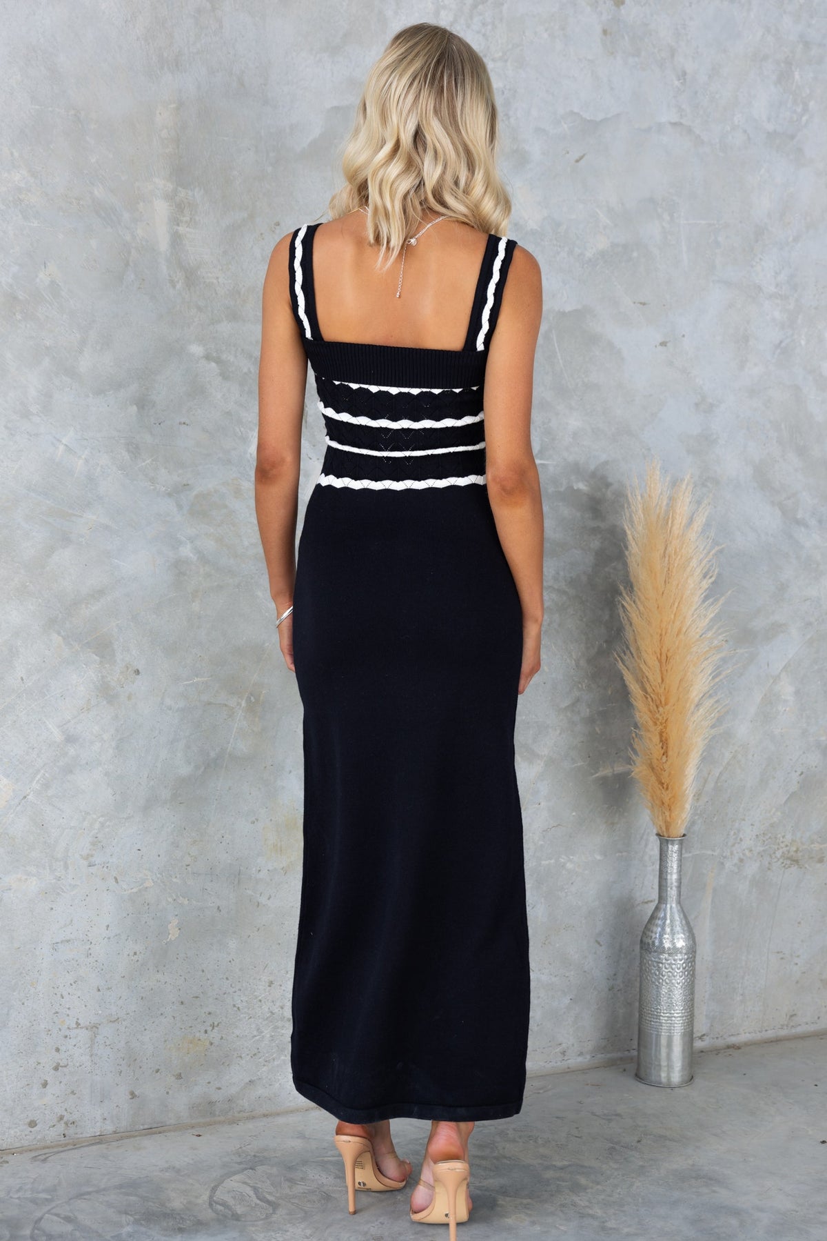Back view of a woman in a black Tarnya maxi dress with white detailing, perfect for summer events.