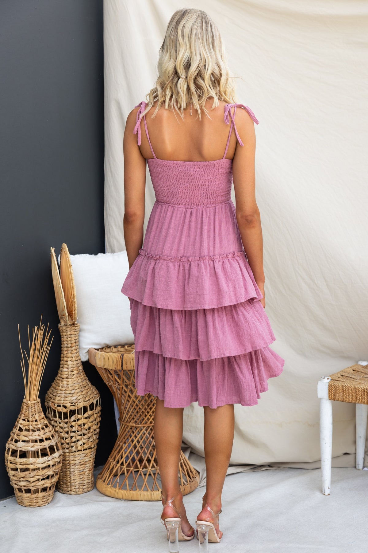 Back view of a woman in a pink Clydie Midi Dress with adjustable straps and tiered layers, styled in a bohemian setting.