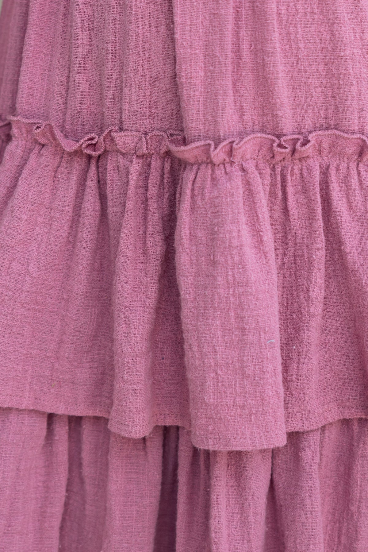 Textured pink fabric detail of the Clydie Midi Dress showcasing ruffled tiers and gathered seams.
