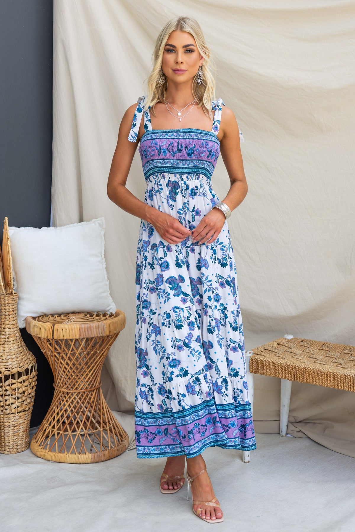 Model wearing Adios Maxi Dress with adjustable tie straps, featuring floral patterns and an elastic bodice, set in a stylish indoor scene.