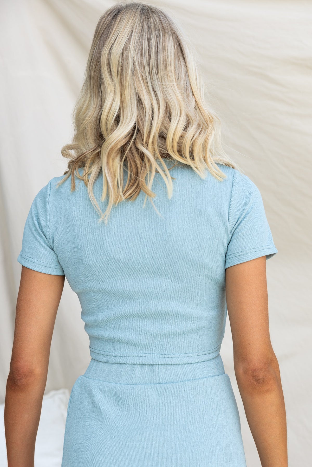 Back view of a woman in a light blue Orian Top with a round neckline and textured material.