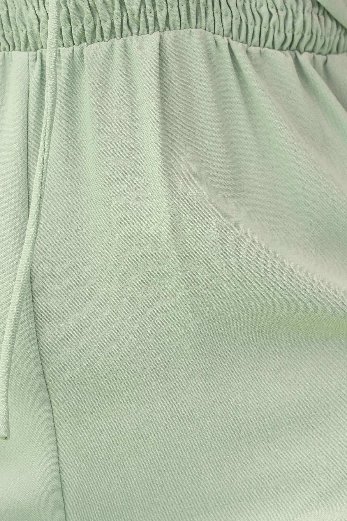 Close-up of the light green fabric of the Nessa Jumpsuit featuring elastic waistband and drawstring detail.