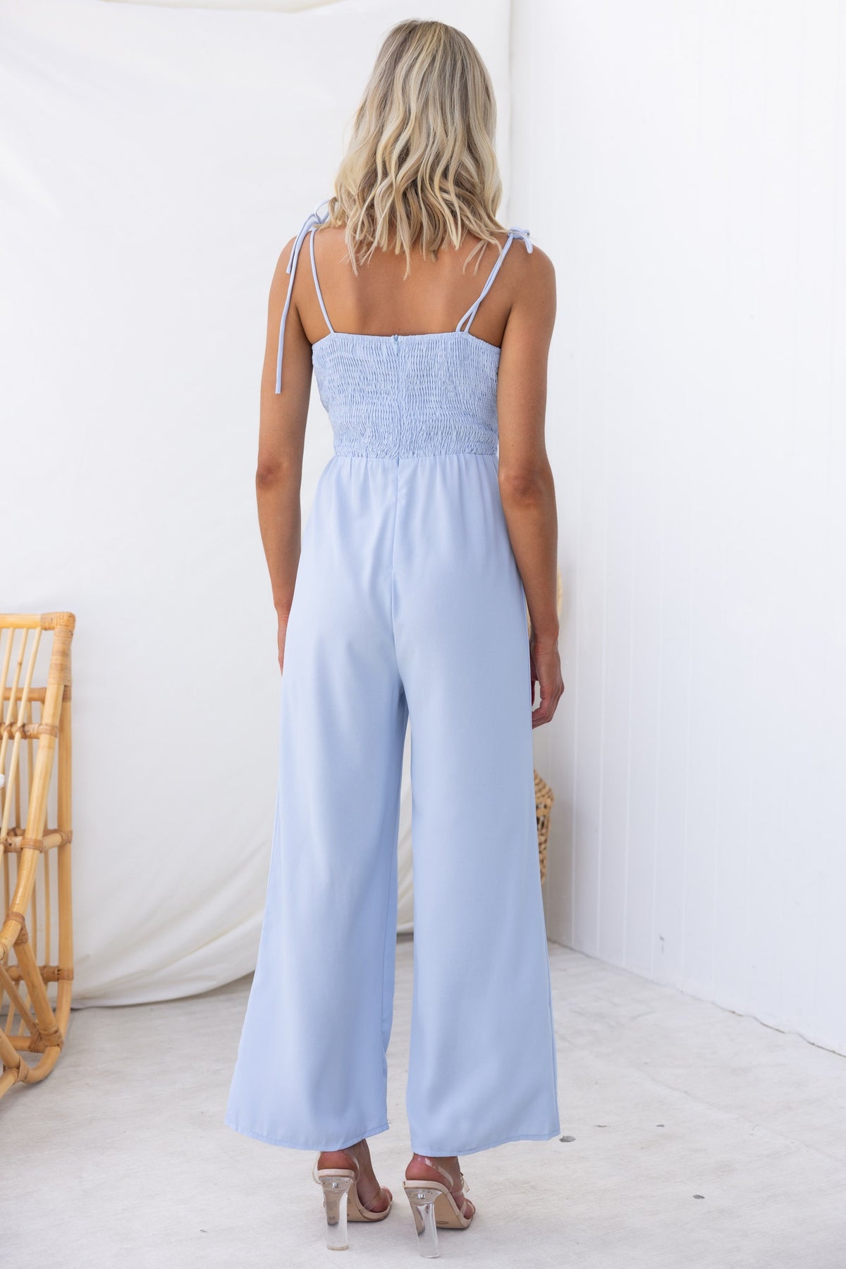 Back view of a woman in a light blue Nessa jumpsuit with adjustable straps and tie detail at the bust.