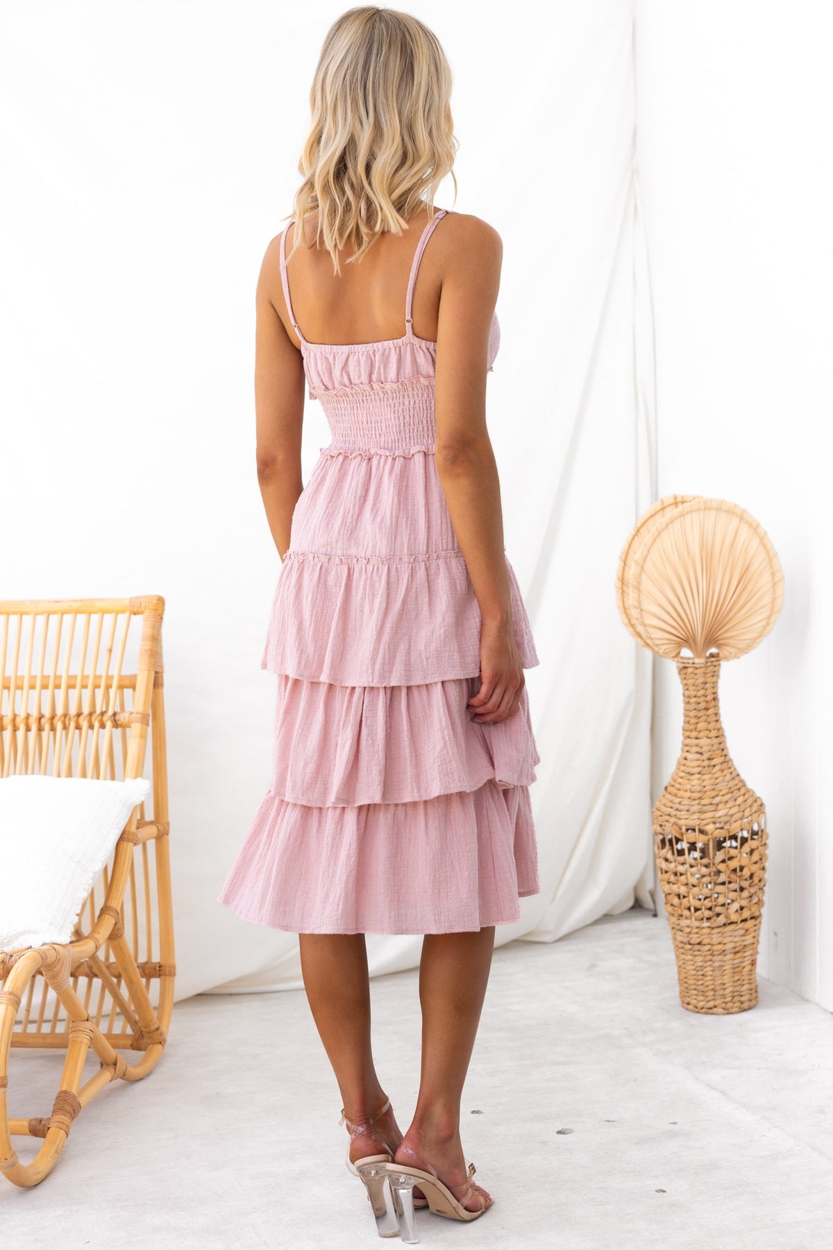 A woman in a pink Jorge Midi Dress with adjustable straps, featuring a tiered design and elastic waistband.