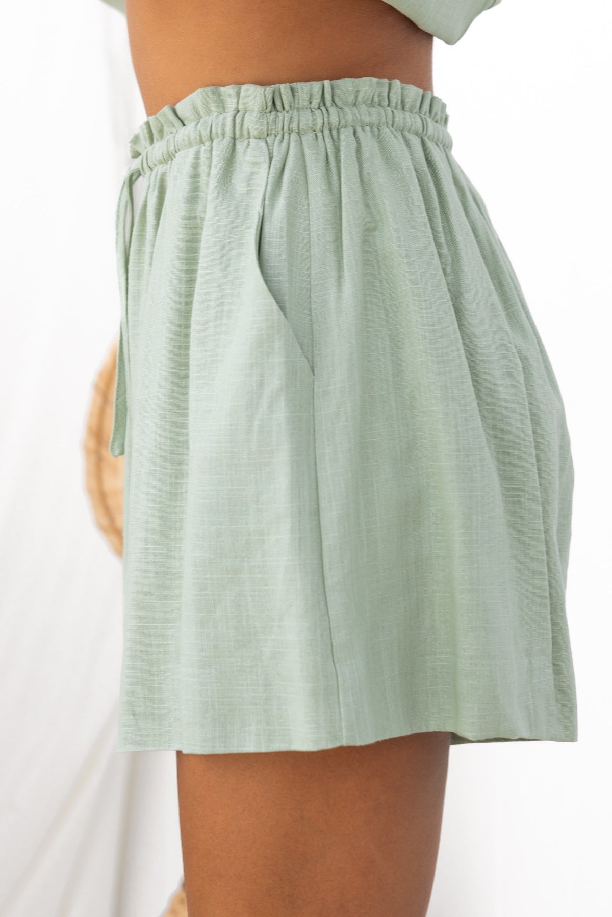 Side view of Vanna Shorts in soft green, featuring elastic waistband, drawstring, and pockets.