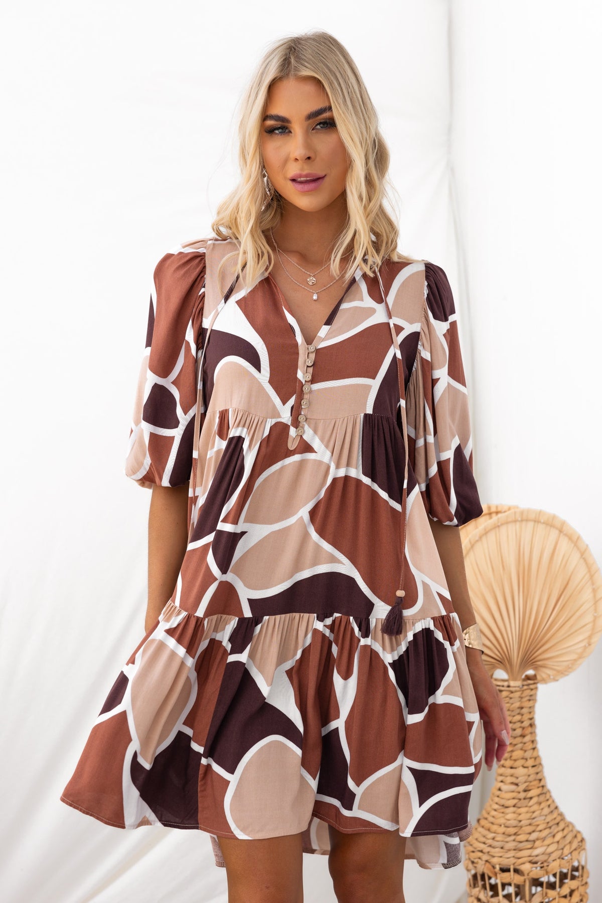 Alisti Dress featuring a V-neckline and tie detail, styled in a brown and cream pattern, perfect for casual outings.