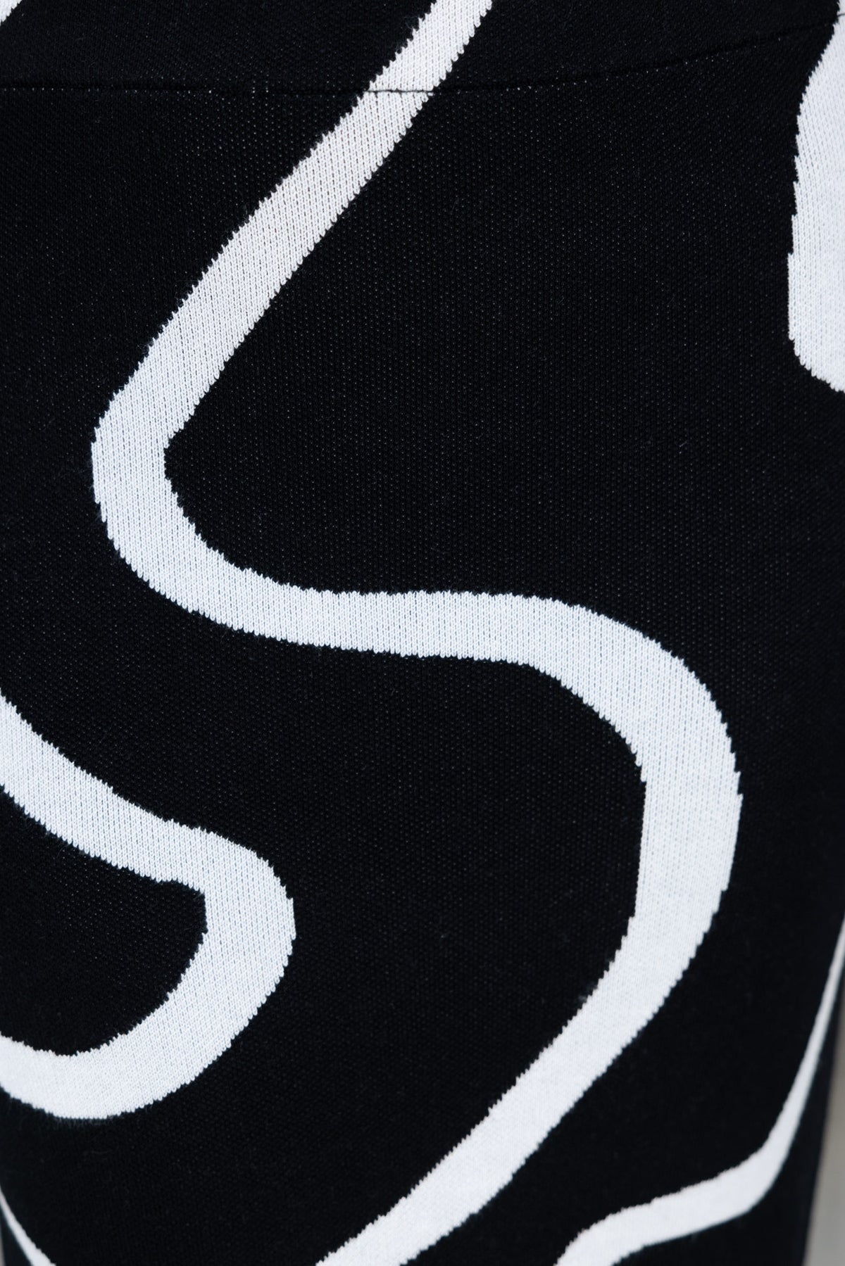 Close-up of a black knit fabric featuring white abstract swirl patterns, highlighting its stretchy texture.
