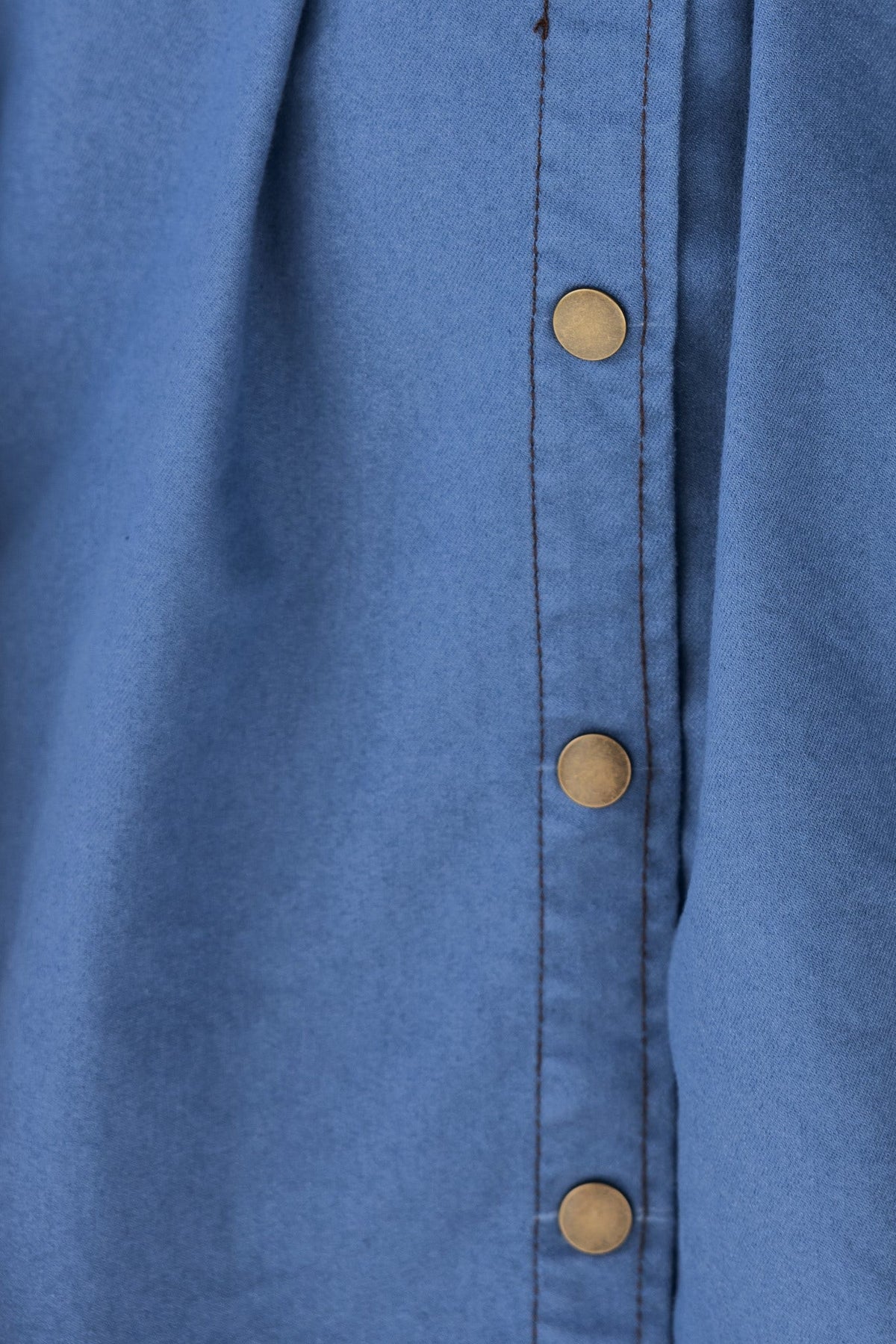 Close-up of the button-up front of a Karsha denim dress in blue, showcasing fabric texture and brass buttons.