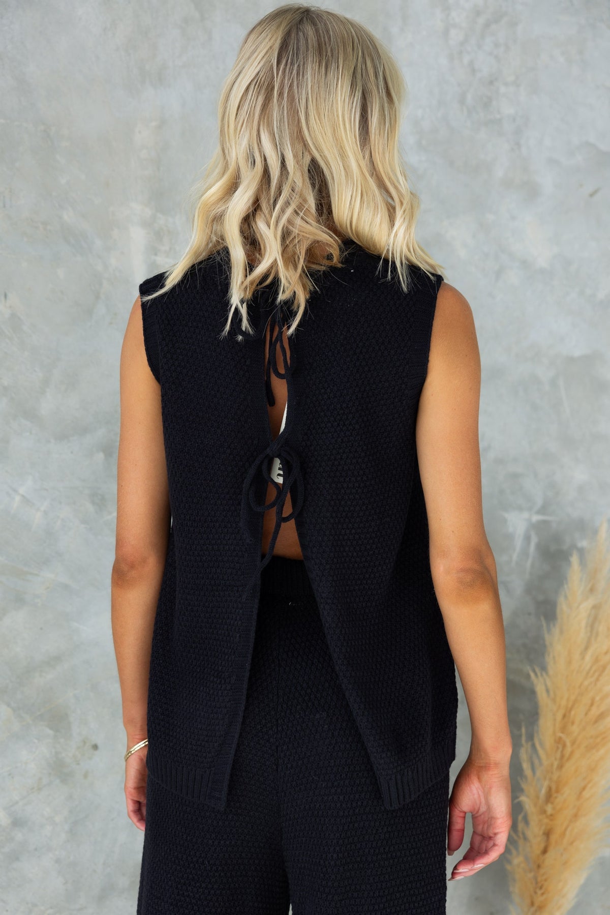 Back view of a stylish black Aera Top, featuring a high neckline and open back with tie details.