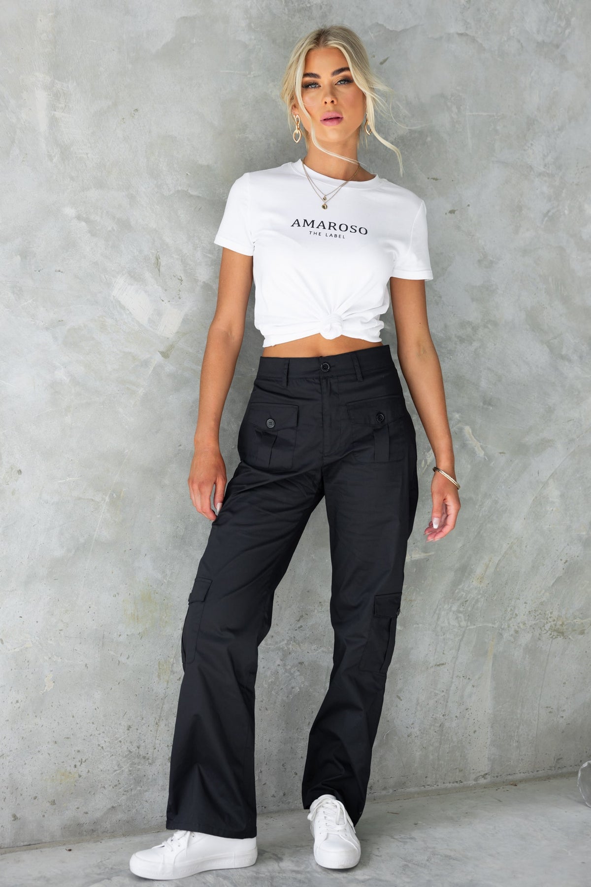 Model wearing Tyrin Cargo Pants in black, styled with a white crop top, showcasing pockets and a mid-waist fit.