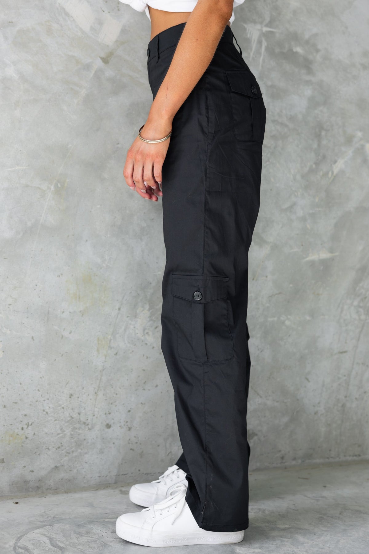 Side view of black Tyrin cargo pants with pockets, worn with a cropped top and white sneakers.