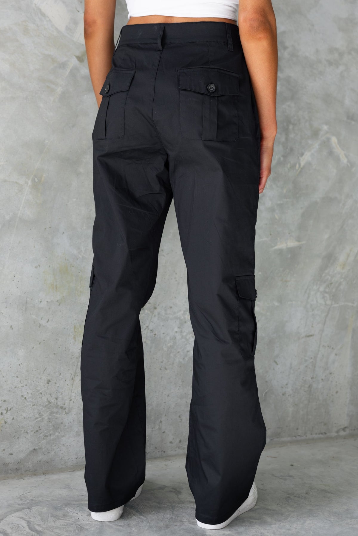 Black cargo pants featuring a high-mid waist fit and multiple pockets, styled from the back.
