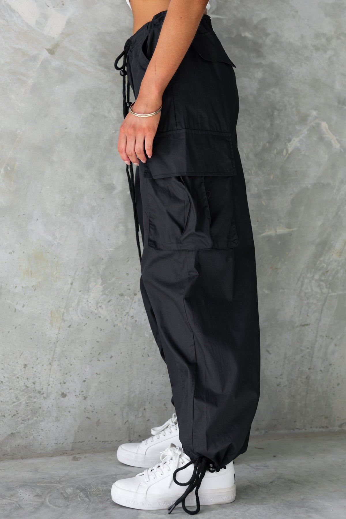 Black cargo pants with wide legs and drawstrings at waist and ankles, styled with white sneakers.