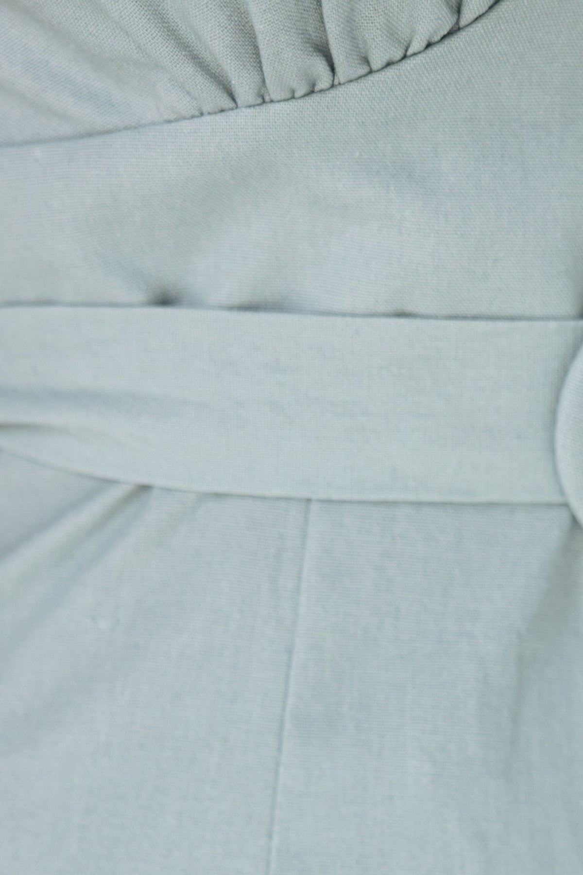 Close-up of the Takk Jumpsuit showing the textured V-neckline and removable belt in soft green fabric.