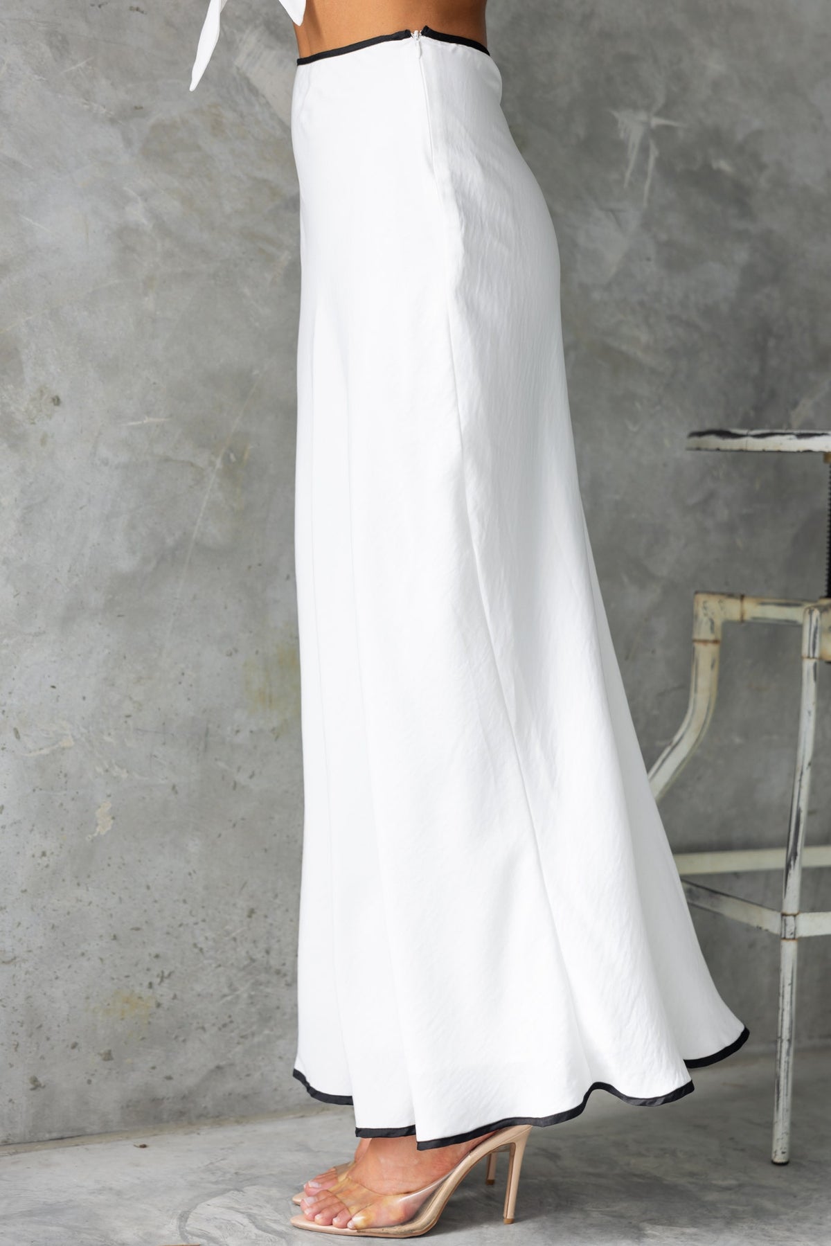 Side view of the Virage Maxi Skirt in white, featuring a mid-high waist and lined design with a contrasting black trim.