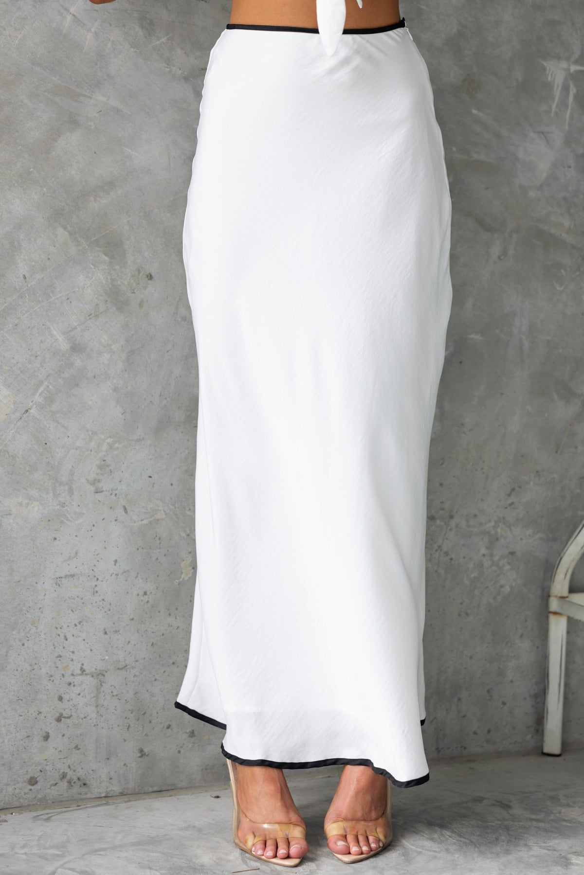 Elegant white maxi skirt with black trim, featuring a mid-high waist and side invisible zip for a chic summer look.