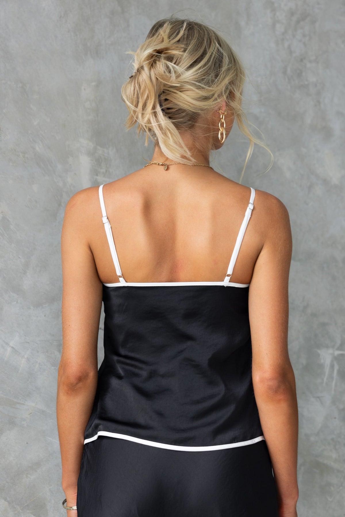 Back view of a woman wearing the Virage Top, a black sleeveless top with adjustable straps and white trim.