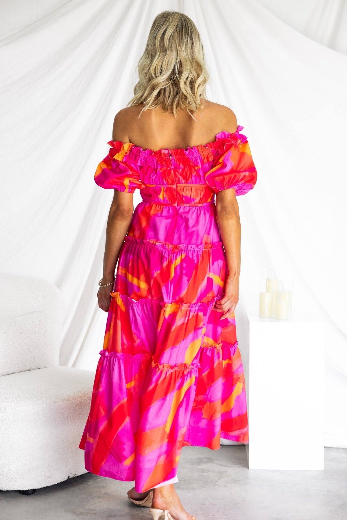 Model wearing a vibrant pink off-shoulder maxi dress with tiered ruffles, highlighting a stylish summer look.