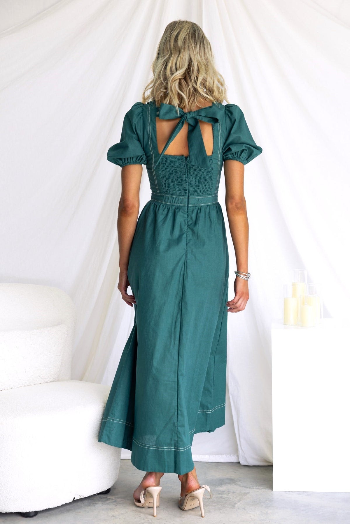 Woman wearing a teal Binita Maxi Dress with a tie back and puffed sleeves, showcasing the elegant rear design.