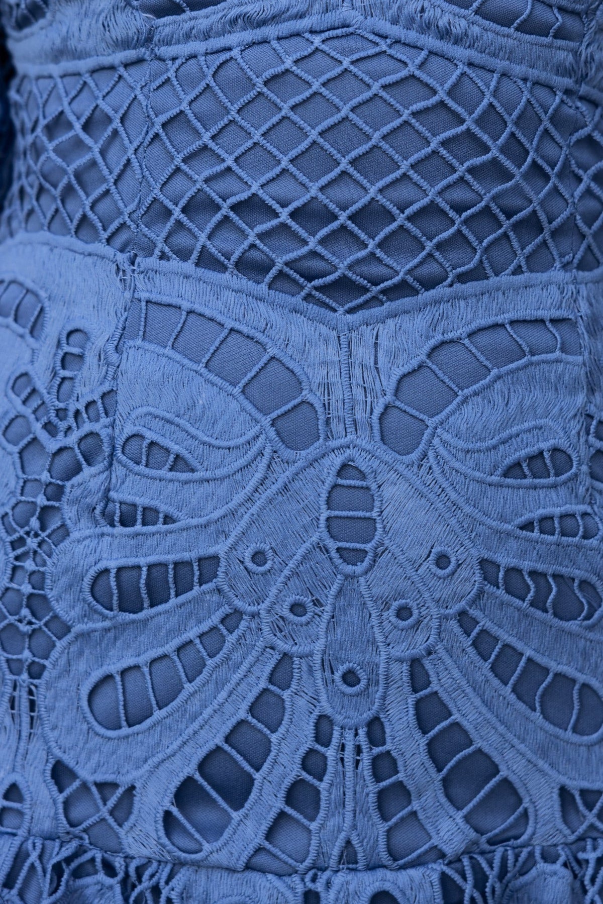 Detailed lace fabric close-up of the Velenia Dress in blue, showcasing intricate patterns and textures.