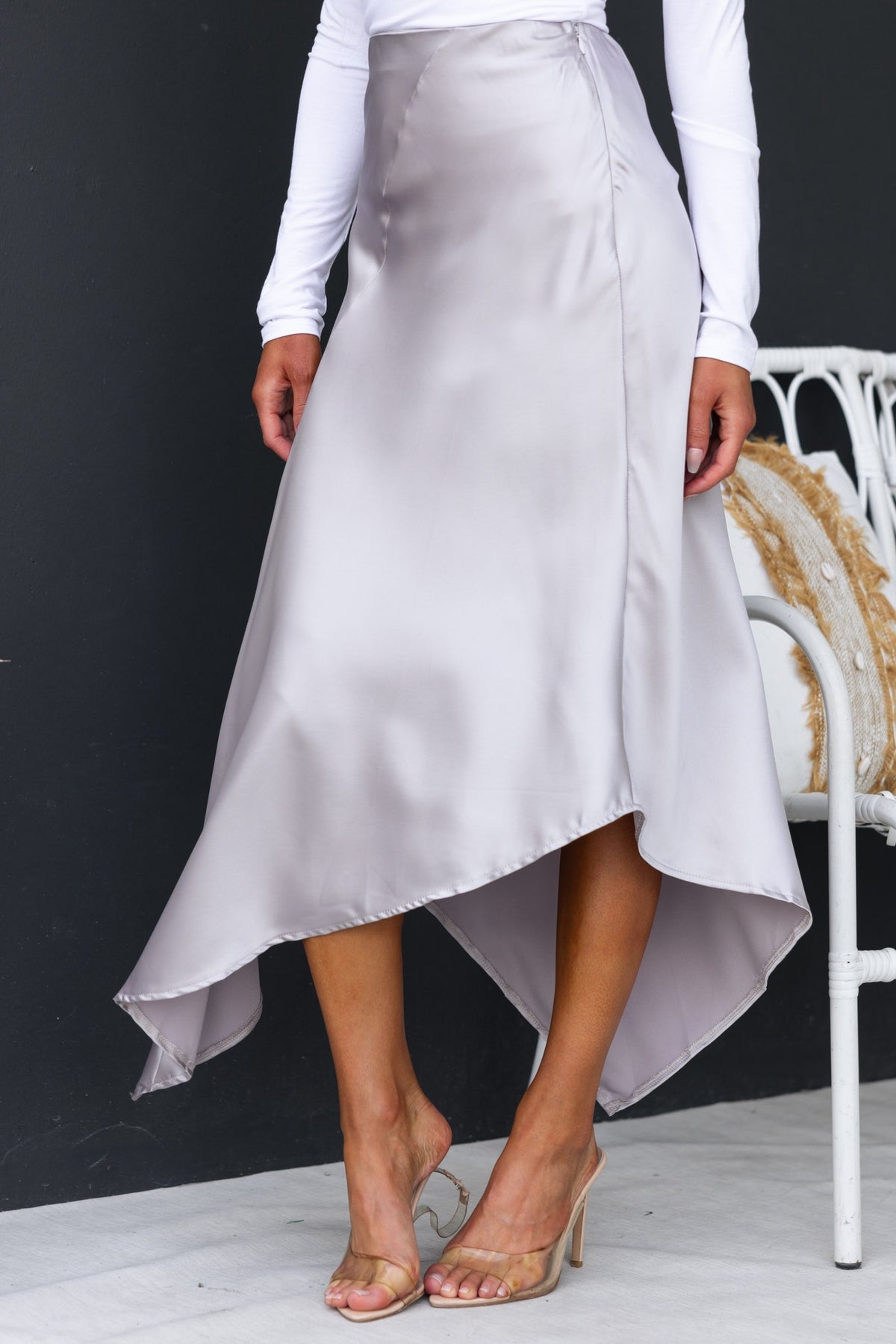 Elegant satin midi skirt featuring an asymmetric hemline and side zip, styled with a fitted top and sandals.