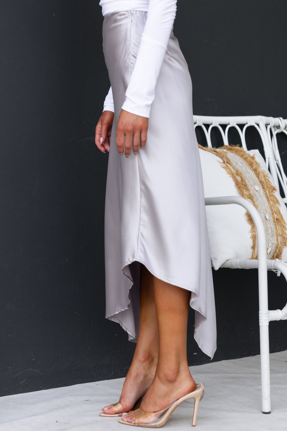 Model wearing a Giallo Midi Skirt with an asymmetric hemline and satin finish, styled with clear heels.