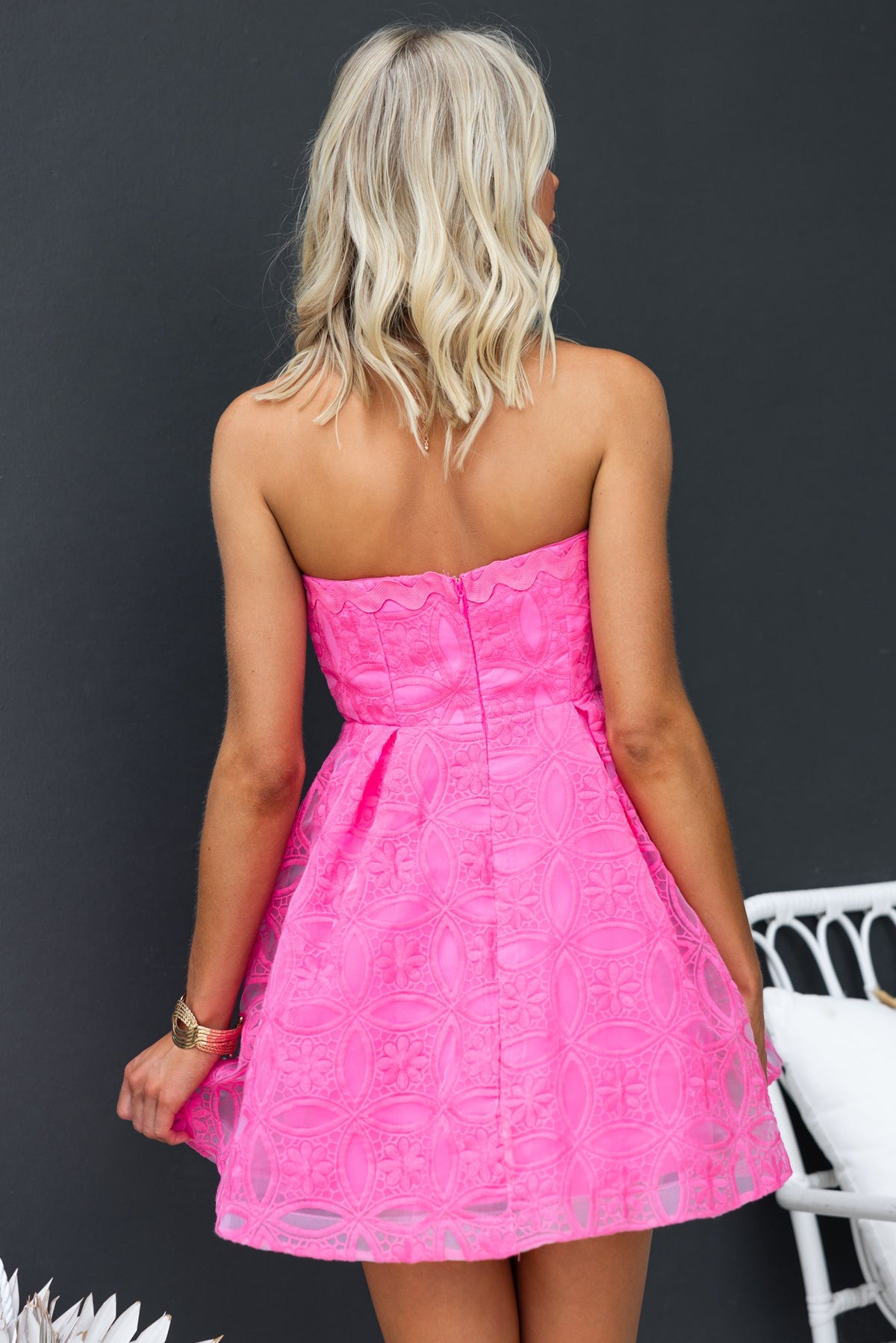Back view of the strapless Millicent Dress in bright pink with a textured lace design and flared skirt.