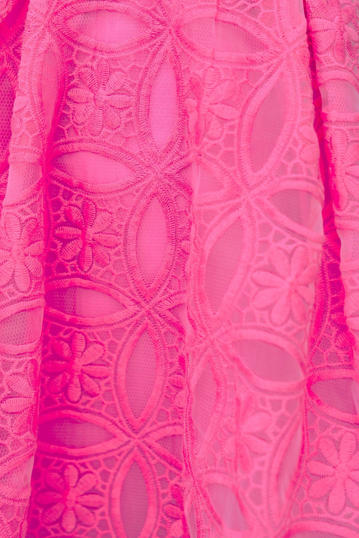 Close-up of vibrant pink lace fabric featuring floral patterns, showcasing delicate details of the Millicent Dress.
