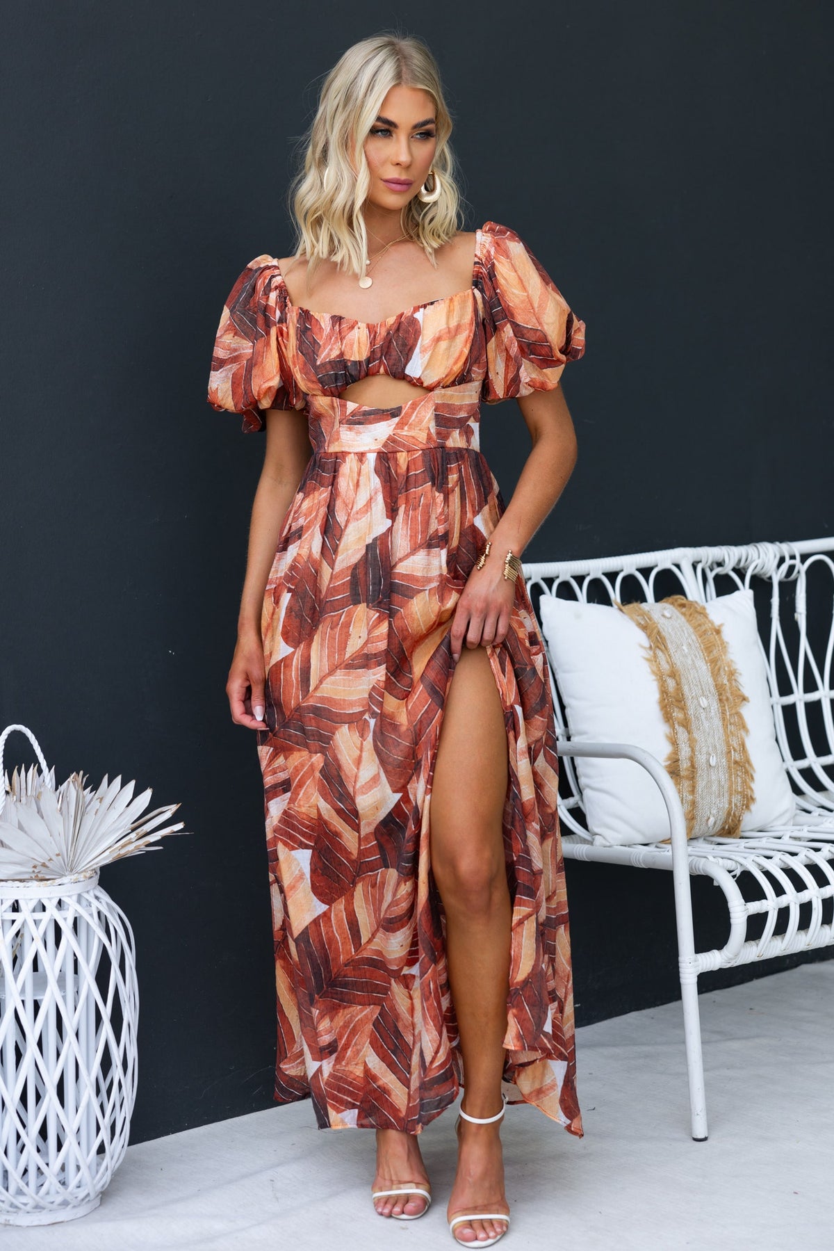 Model wearing Damaris Maxi Dress with puff sleeves and front split, featuring a bold leaf print against a dark background.