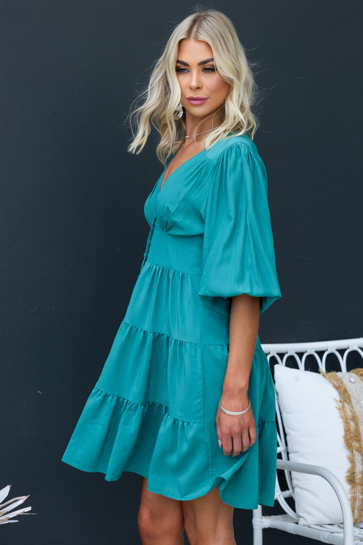 Model wearing the Damika Dress in teal with V-neckline, button-up front, and puff sleeves.
