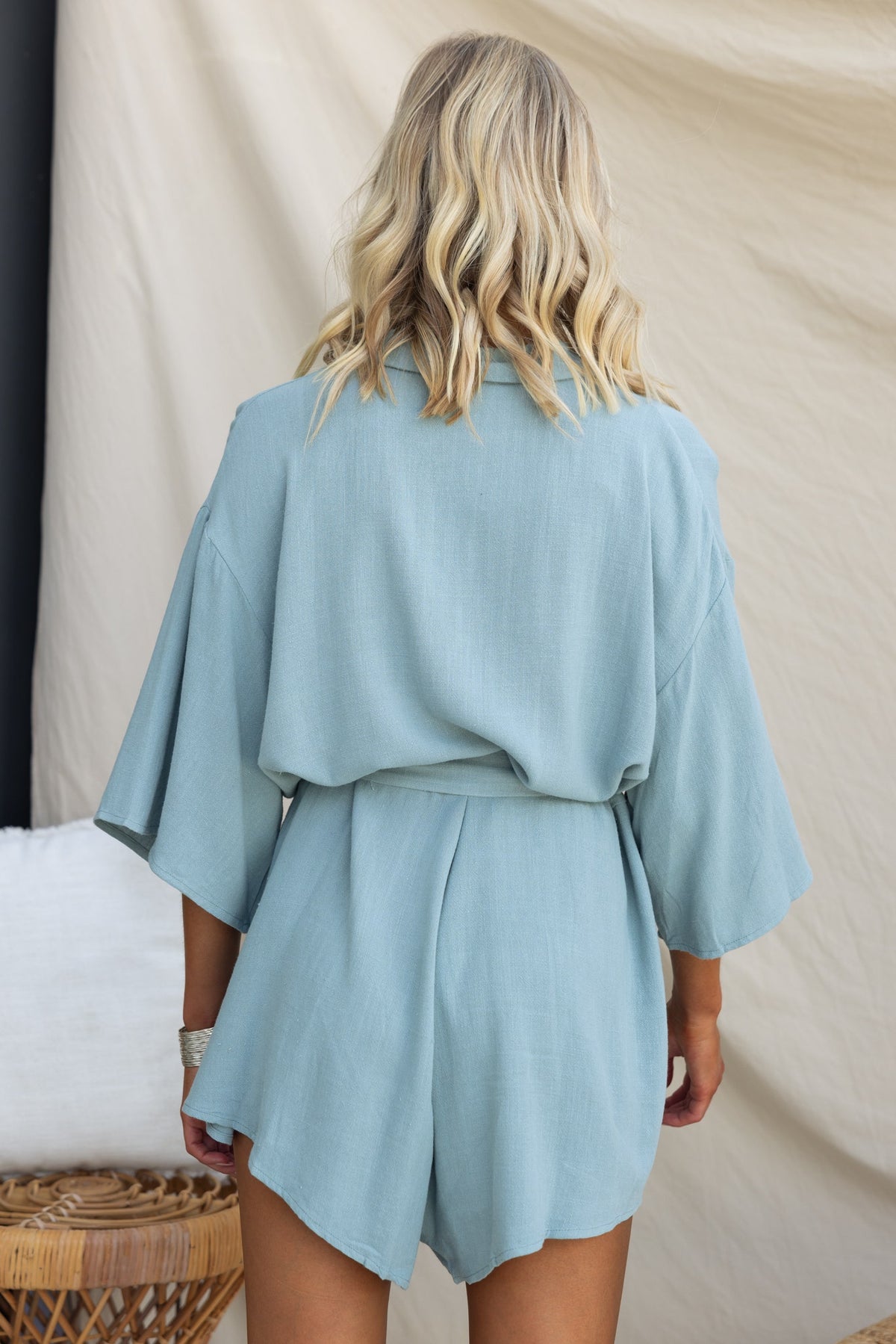 Back view of a model in a relaxed fit Wyoma Playsuit, featuring short sleeves and a soft blue linen look.