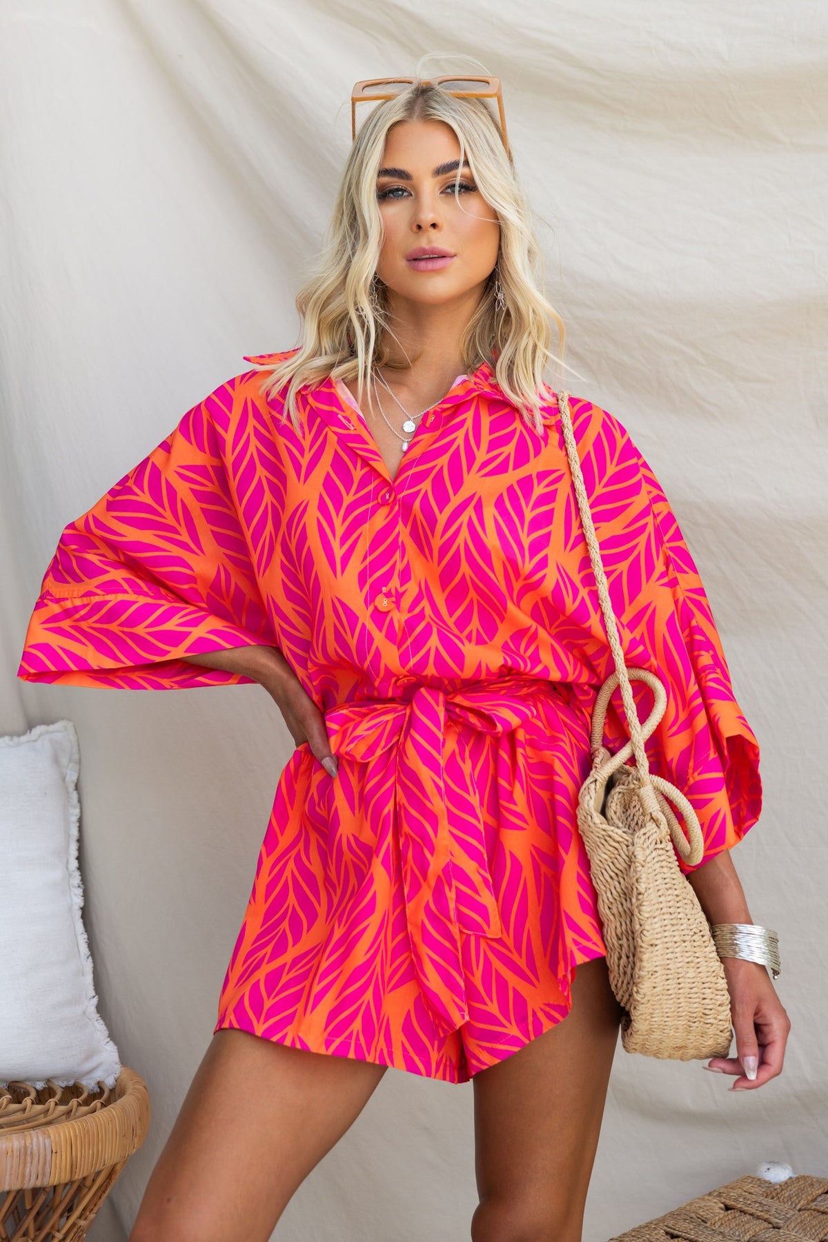 Hollis Playsuit in vibrant pink leaf print, featuring a button-up collar, removable belt, and relaxed fit.