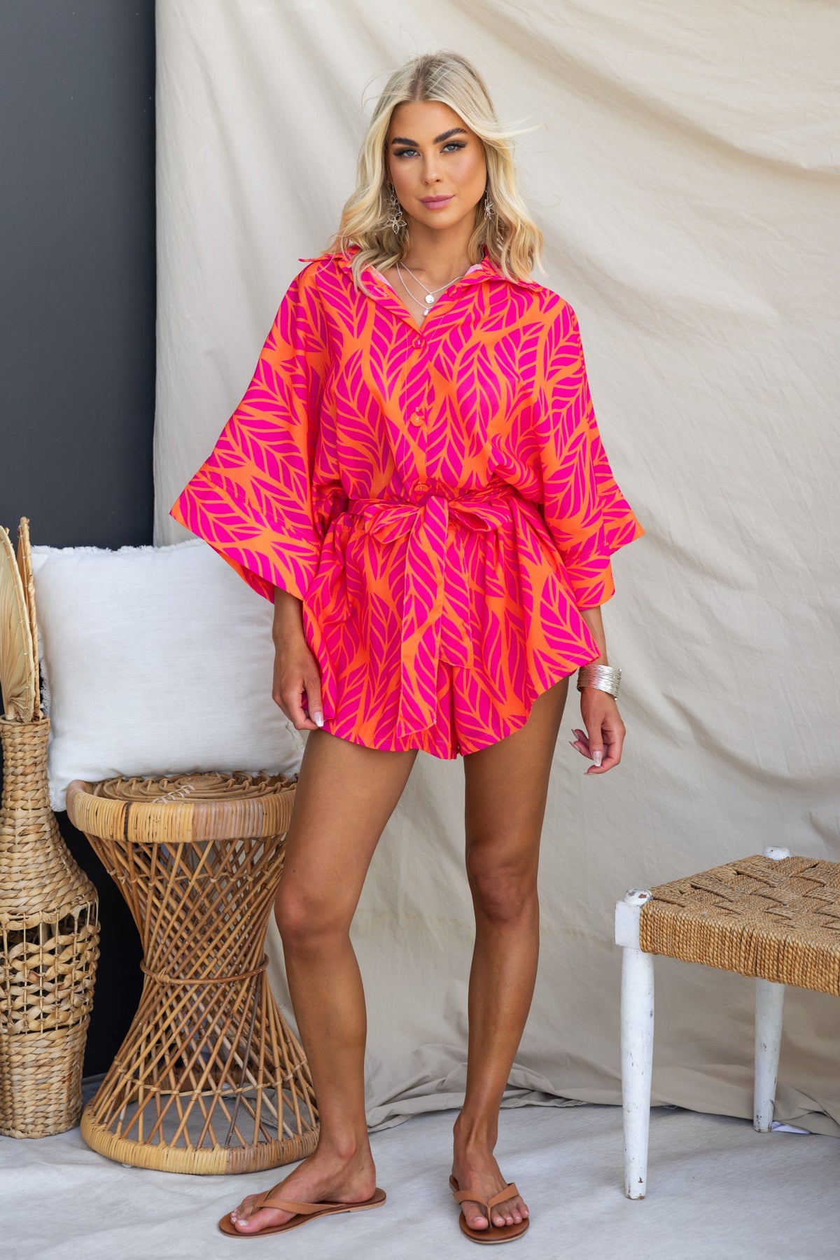 Bright pink Hollis playsuit with leaf print, button-up front, and removable belt, styled for a relaxed fit.