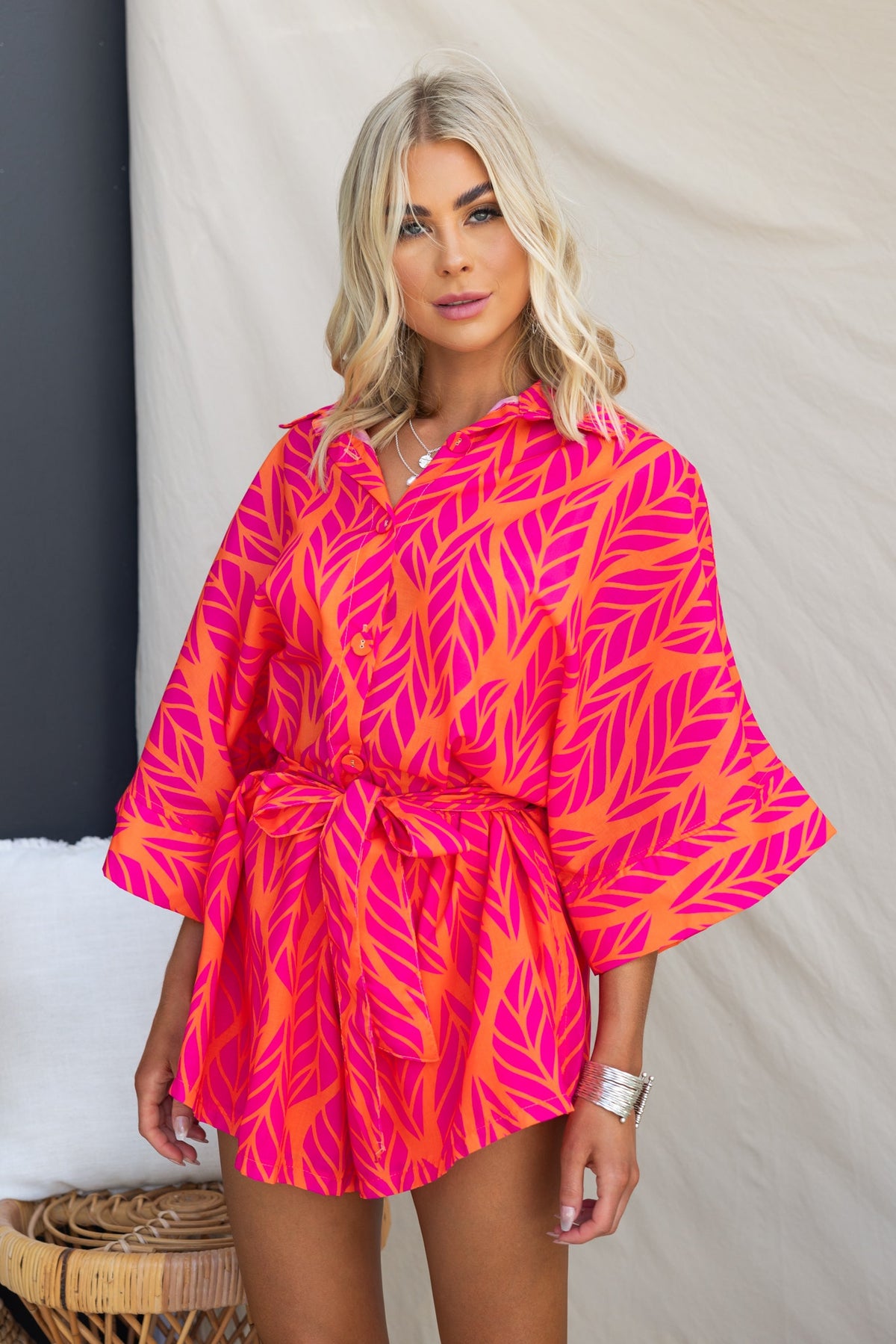 Bright pink and orange leaf-patterned Hollis Playsuit featuring a collar, button-up front, and removable belt.
