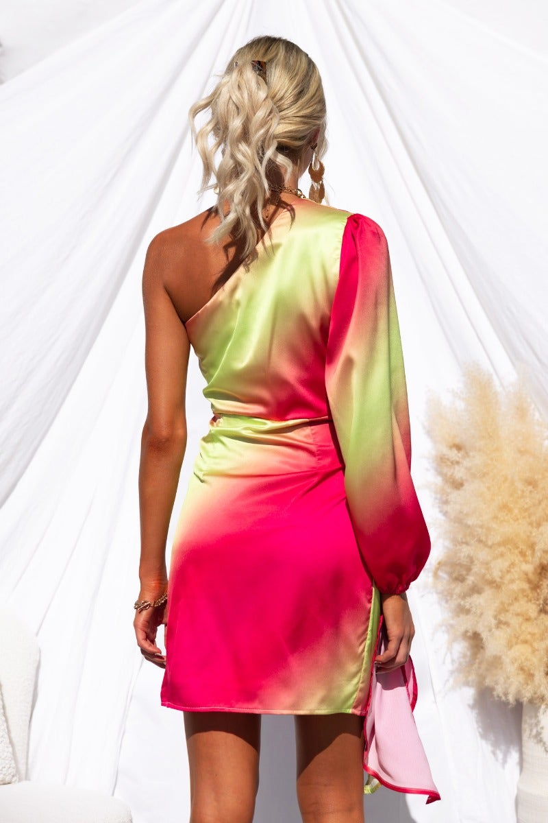 Back view of Tempest Dress with vibrant pink and green satin fabric, featuring a one-shoulder design and flowing sleeve.