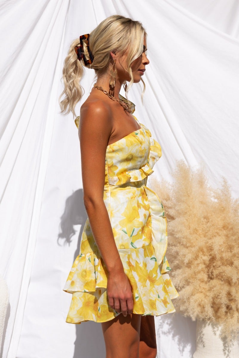 Model in a yellow floral print dress with a ruffle trim and one-shoulder neckline, styled with accessories.