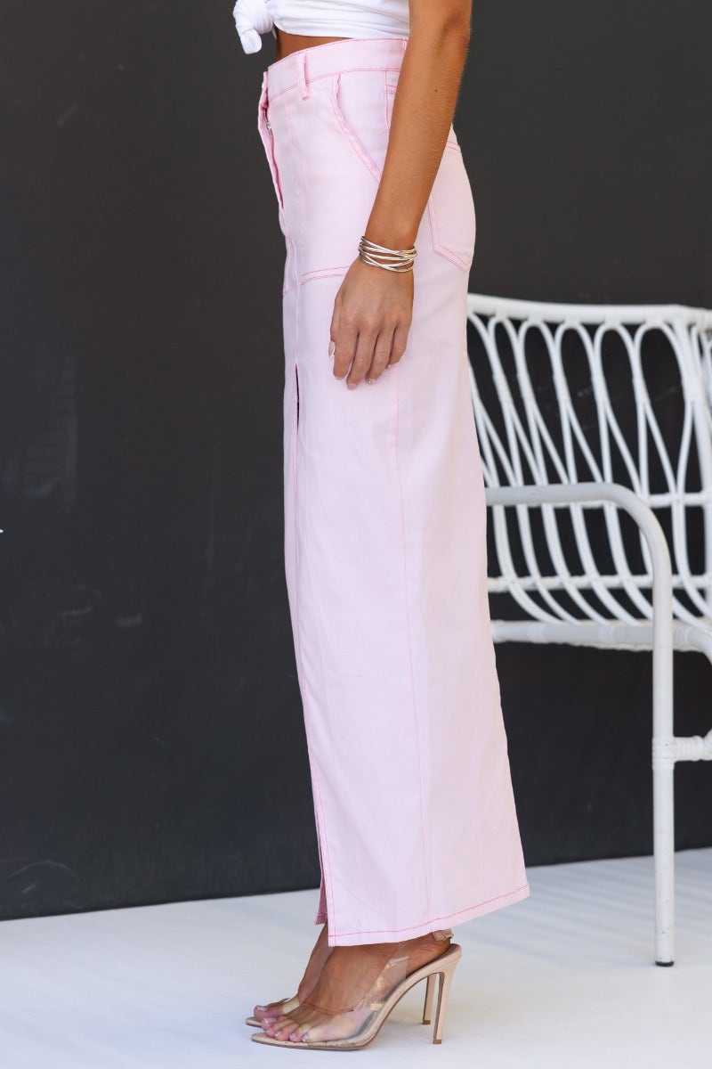 Pink denim maxi skirt featuring a high split, pockets, and mid-low waist fit, styled with a trendy top.
