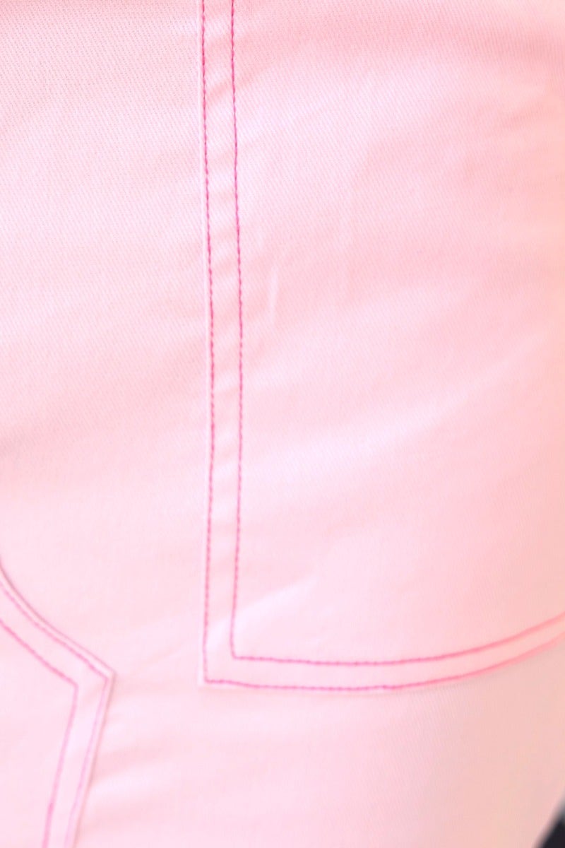 Close-up of pink denim fabric highlighting stitching details and pocket design.