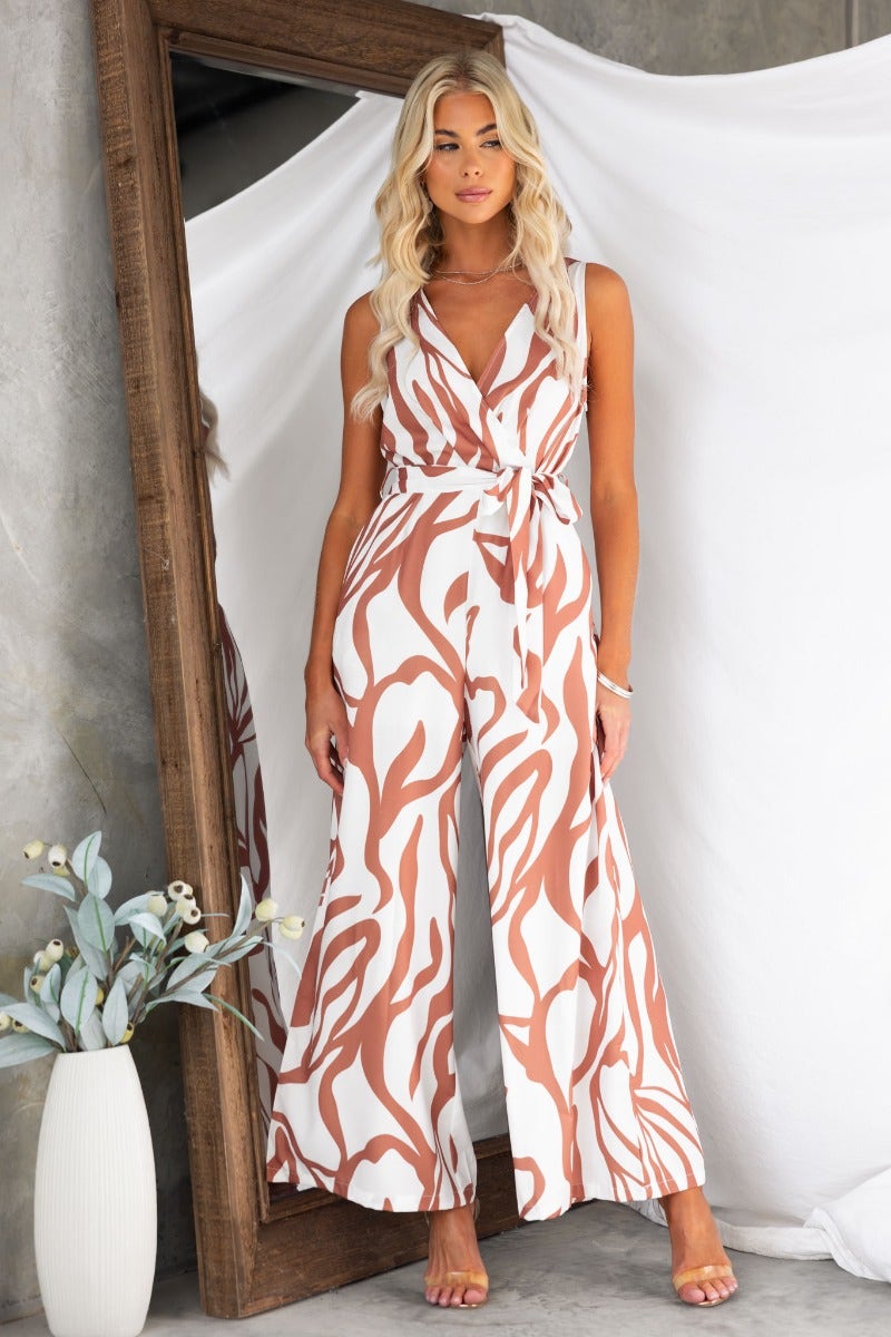 Girl Almighty linen blend jumpsuit with V-neck, side zip, pockets, and removable tie, styled with a mirror backdrop.